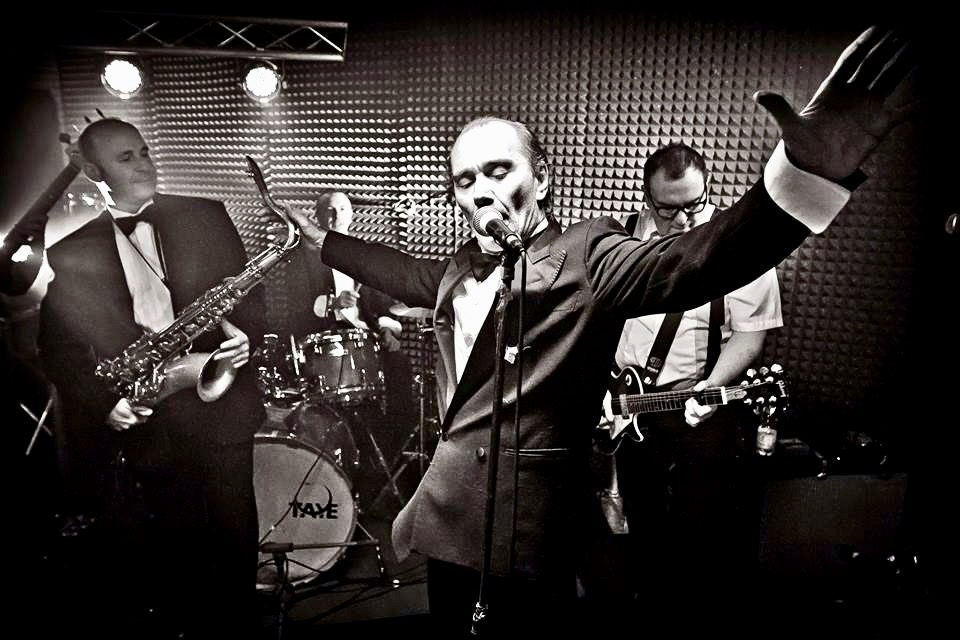 Il cantante a braccia aperte durante un concerto dei Vindicators, con sax e batteria alle spalle